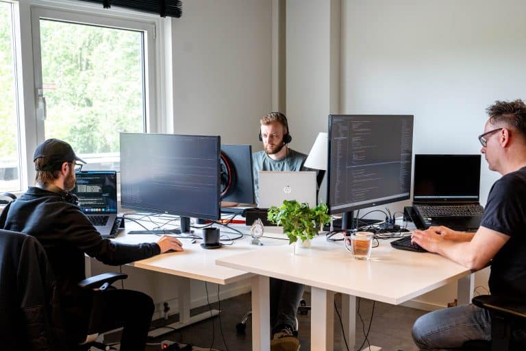 3 developers werken ieder achter een eigen beeldscherm.