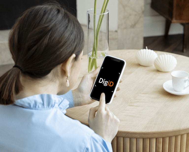 Een vrouw kijkt naar het scherm van een mobiele telefoon. Daarop staat het logo van DigiD. Yard heeft een TPM-verklaring gekregen, zodat gebruikers veilig kunnen inloggen met DigiD in de MijnOmgeving voor gemeentes.